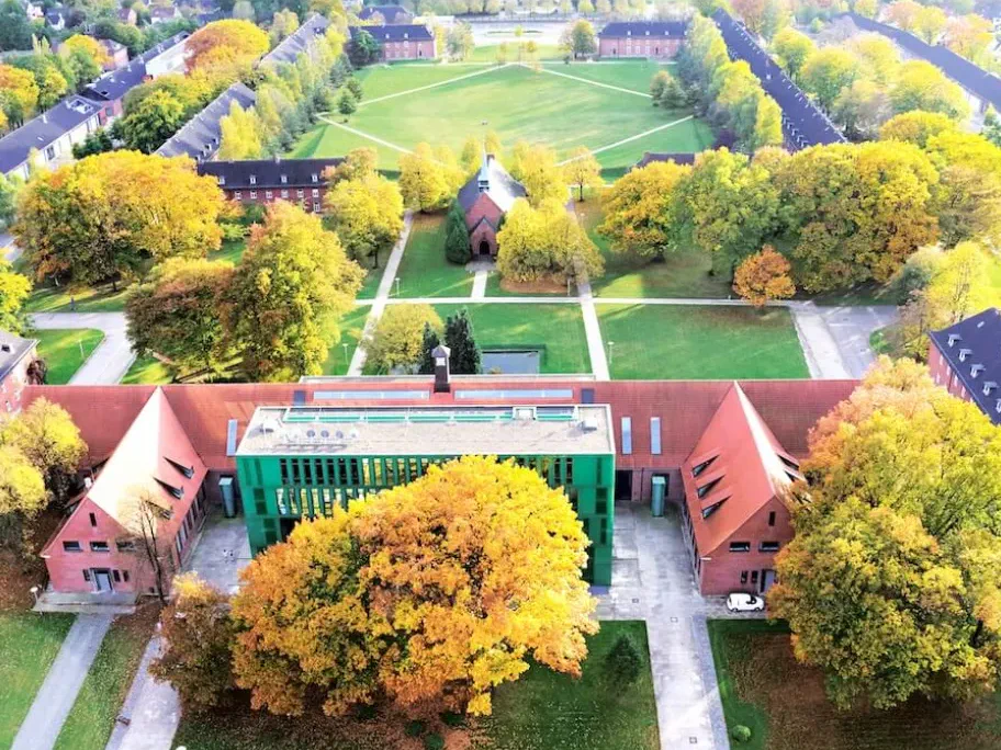 Aerial view of the Constructor University campus in Bremen in autumn, with red-brick buildings around a central lawn and a green glass-fronted building in the foreground.