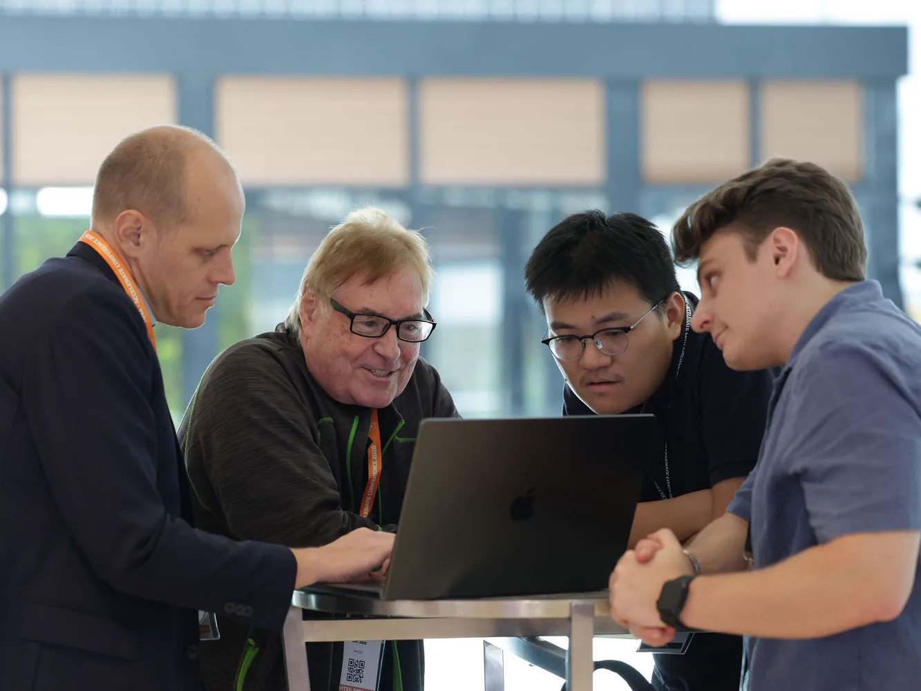 Four AI4X 2026 participants gathered around a laptop in discussion